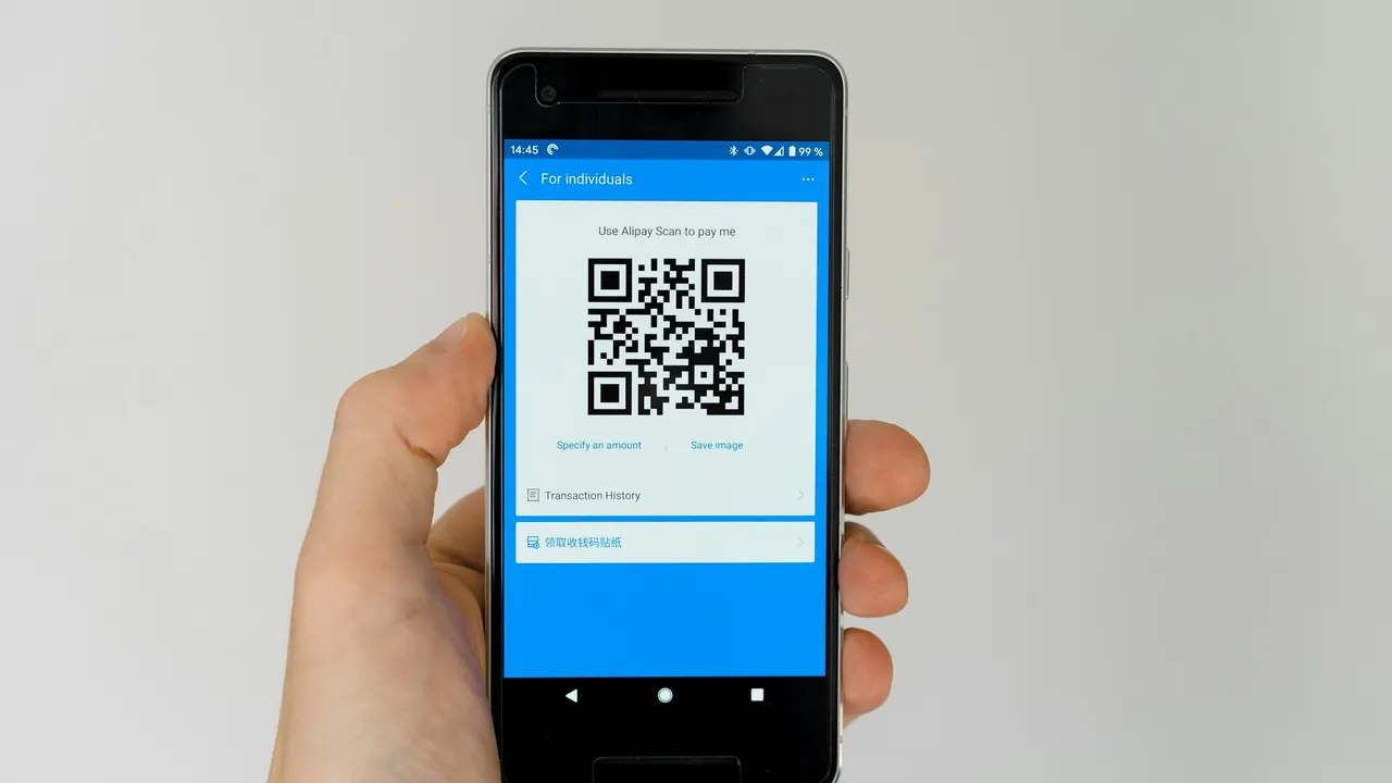 Hand holding a phone displaying an Alipay merchant payment QR code