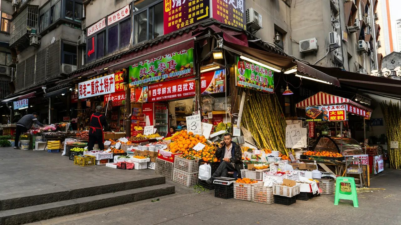 Street fruit shop displaying stacks of oranges, bananas, and sugar cane by outdoor steps.