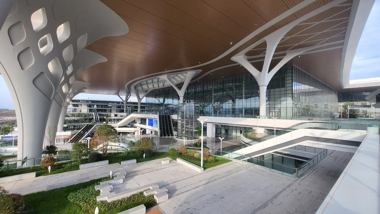Chongqing East station’s covered forecourt, with escalators beside its glass entrance.