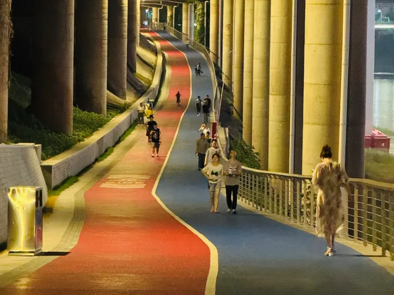 People on the red and blue Beibin Road path beneath illuminated bridge columns at night