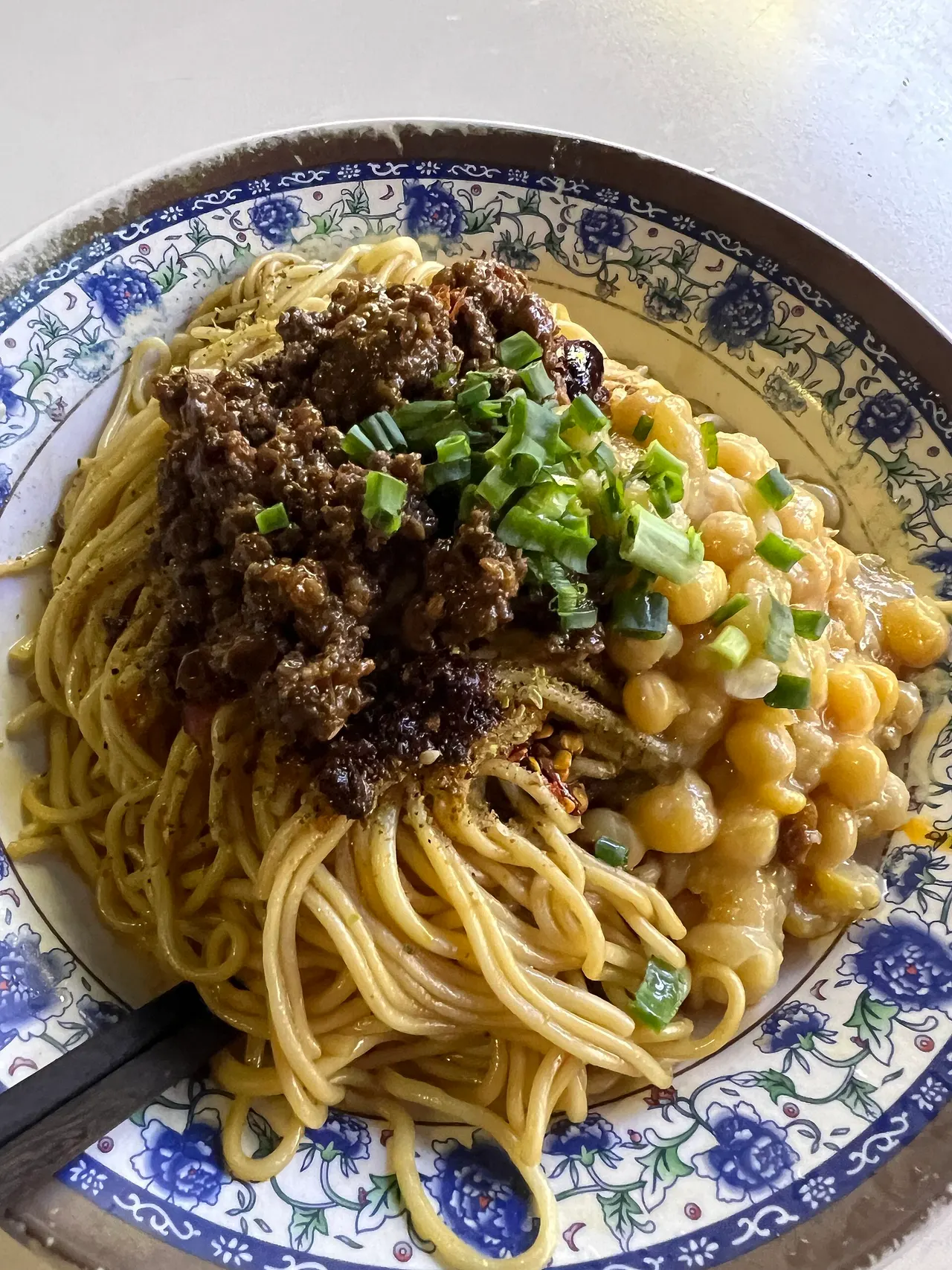 Wan-za noodles topped with yellow peas, minced pork and green onions in a blue-and-white bowl.