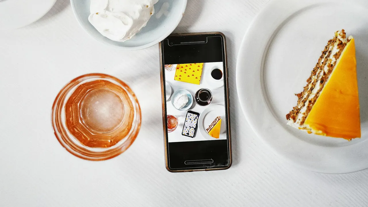 Telefon pintar di sebelah kopi dan kek di atas meja kafe putih