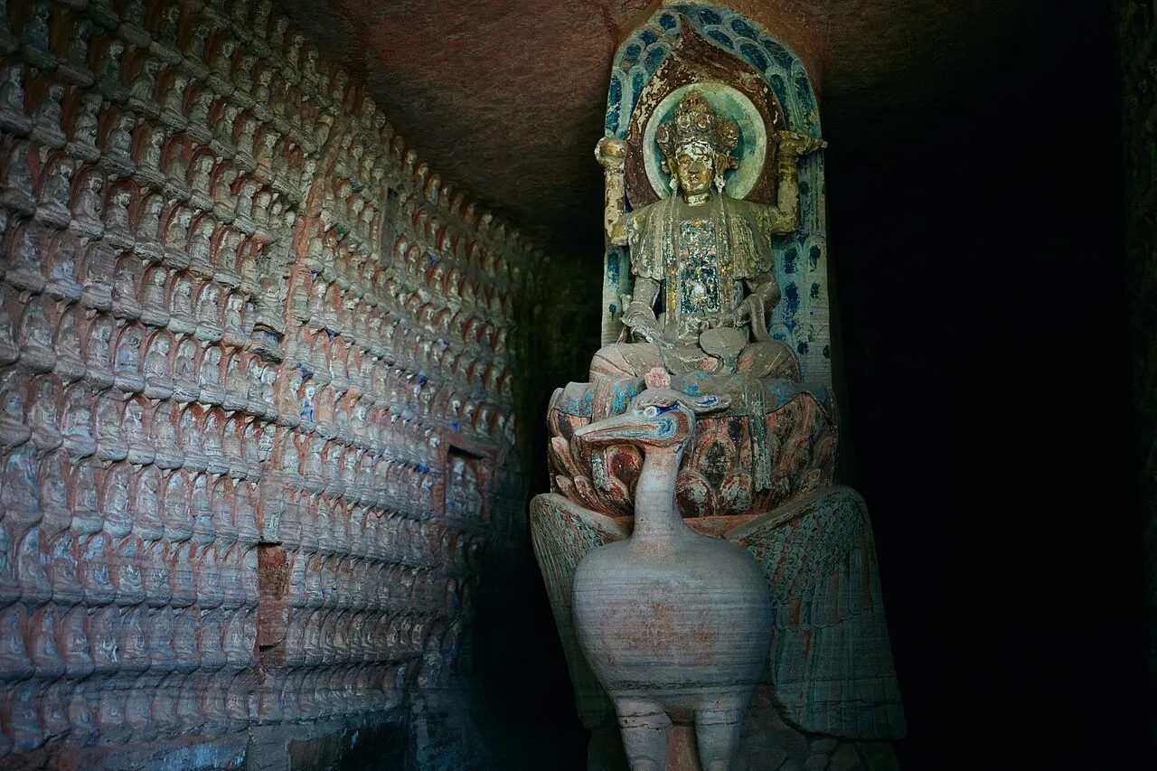 Painted stone sculpture above a peacock beside rows of small Buddhas at Beishan