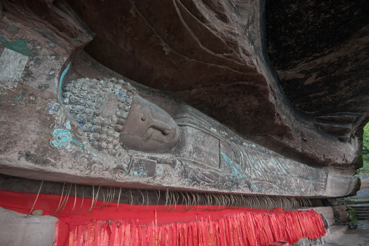 The reclining Buddha carved into the cliff, with blue decoration and red prayer ribbons