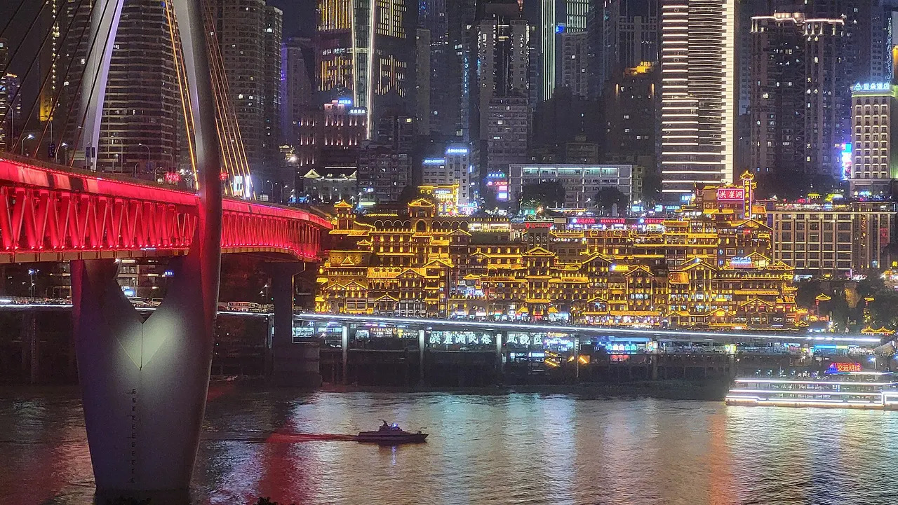 Hongya Cave lit up across the Jialing River, beside Qiansimen Bridge and passing boats.