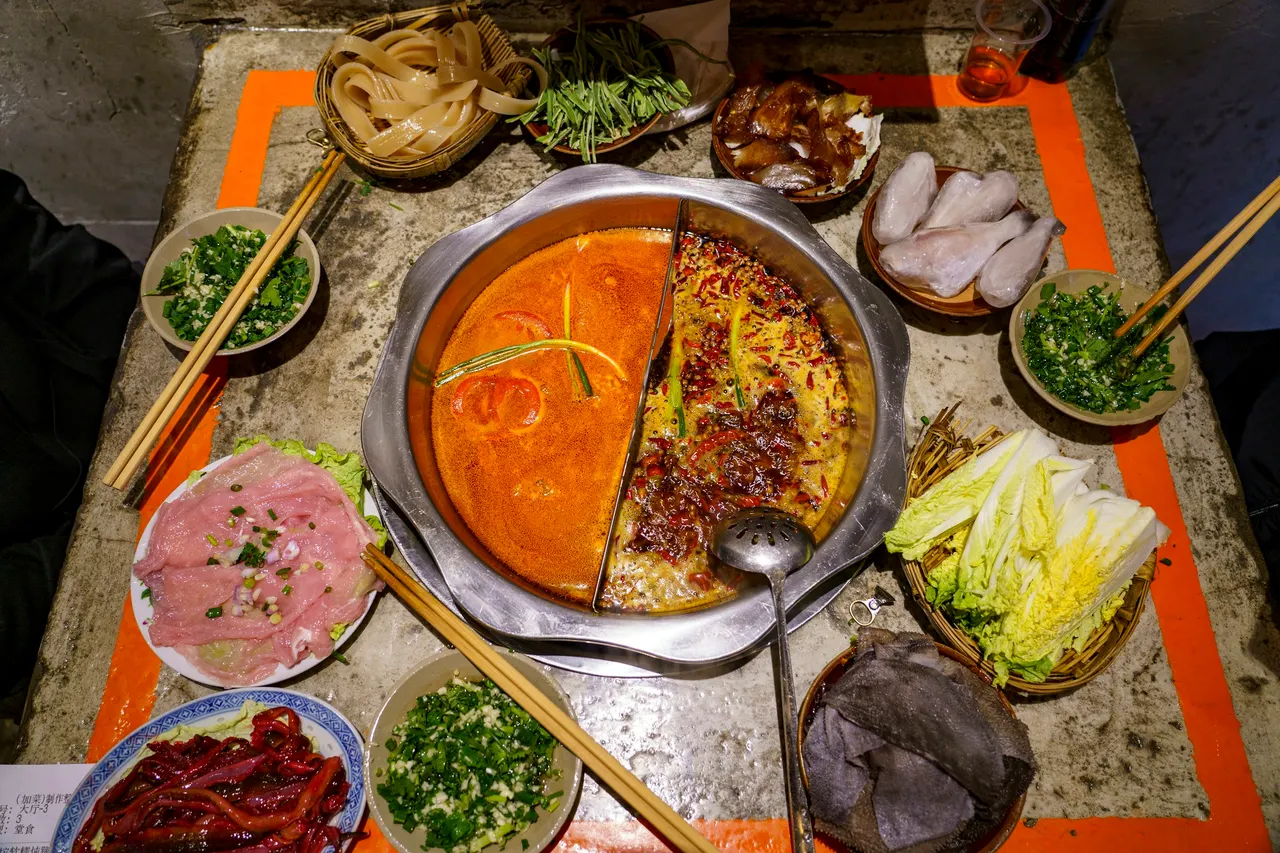 Table set with a split two-flavor hotpot, raw meat, tripe, vegetables, and dipping bowls.