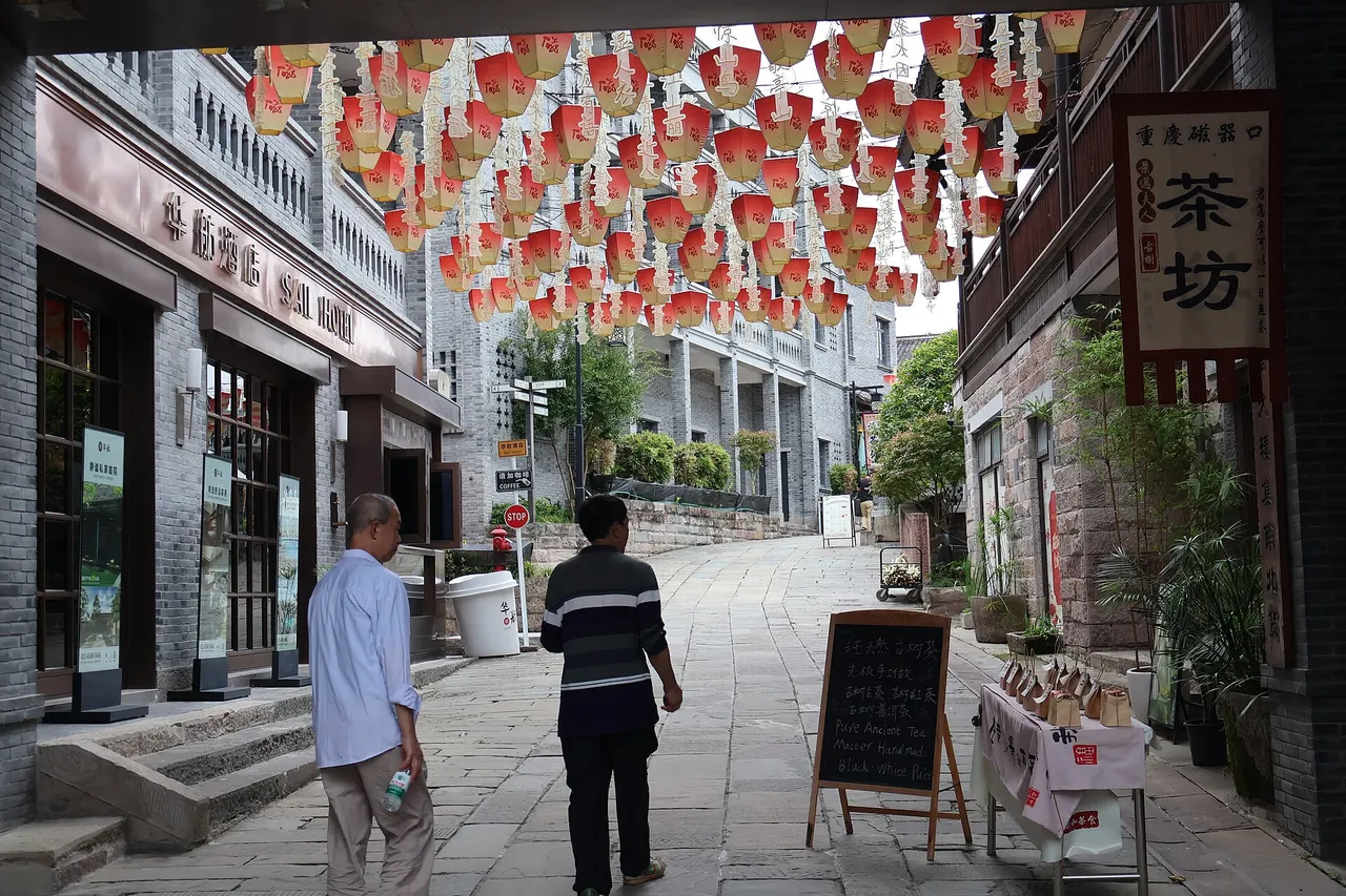 Paved pedestrian alley in Ciqikou lined with lanterns, tea-shop signs, and outdoor tables.