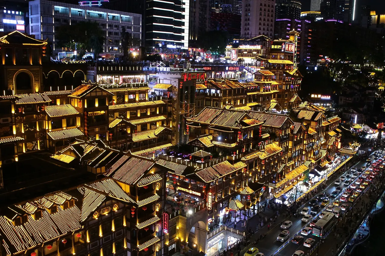 Hongya Cave illuminated at night with its layered eaves and riverside road below.