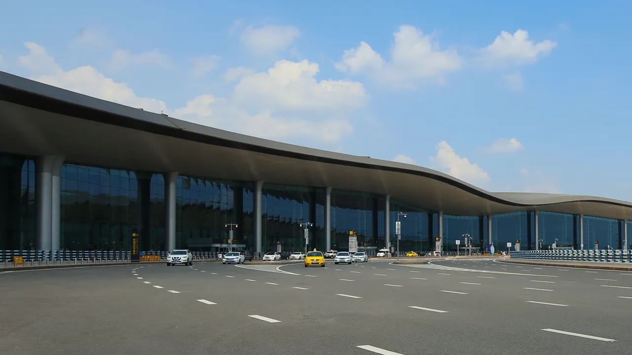 The curved roof and glass facade of Chongqing Jiangbei Airport’s T3A main terminal beside its departure roadway.