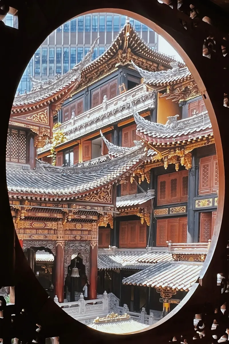 A circular wooden window frames the layered roofs and courtyard buildings of Luohan Temple