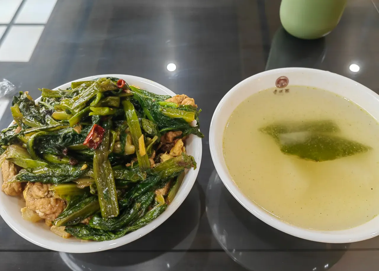A plate of cooked green vegetables and a bowl of light soup on a black table at Luohan Temple