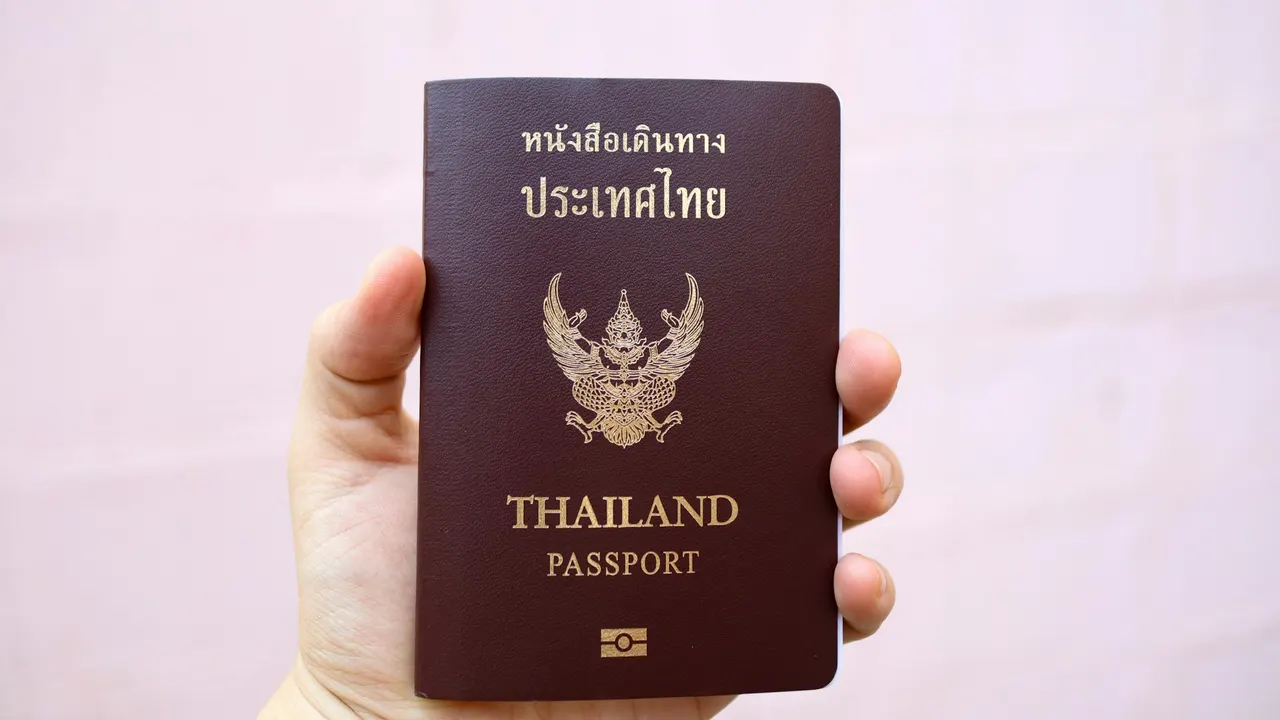 มือที่ถือหนังสือเดินทางไทยบนพื้นหลังสีชมพู
