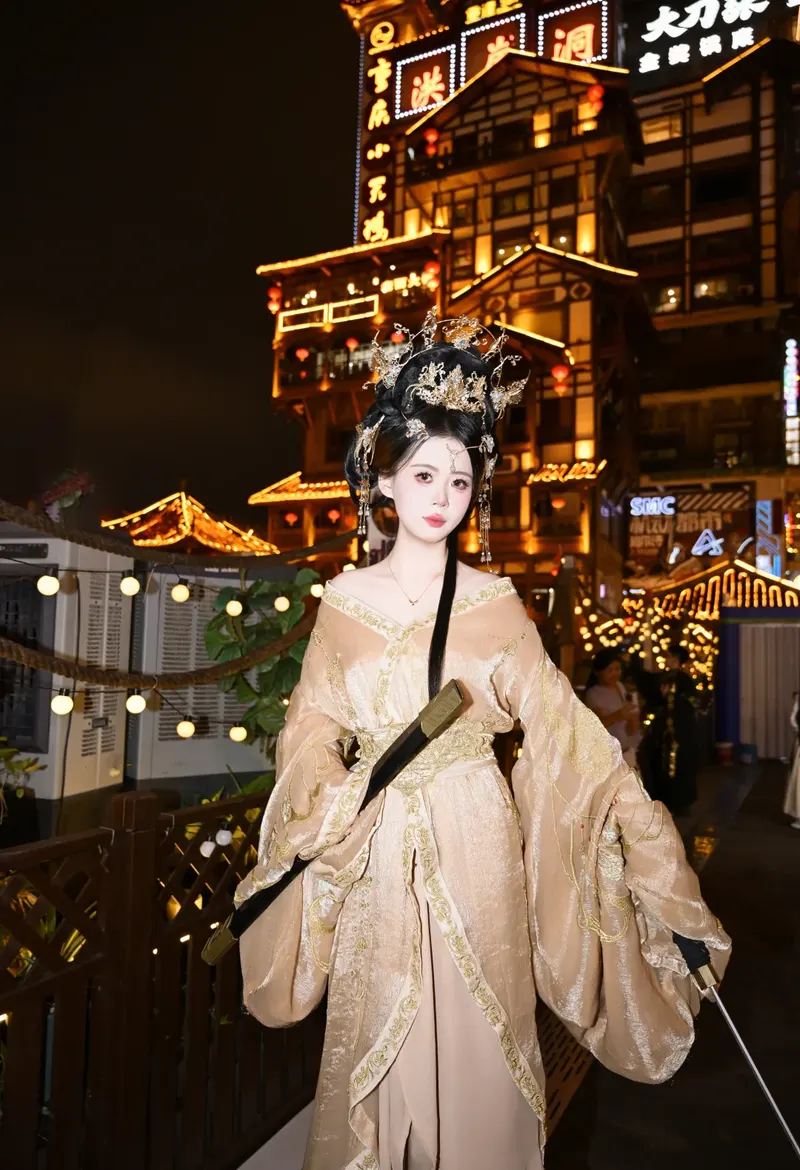 Woman in gold Hanfu holding a prop sword, with Hongya Cave illuminated behind her at night