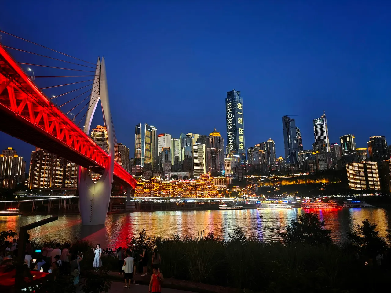 The red Qiansimen Bridge and Hongya Cave light up Chongqing's riverfront at dusk.