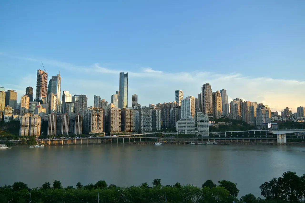 Chongqing's waterfront towers rise above a river under a clear blue sky.