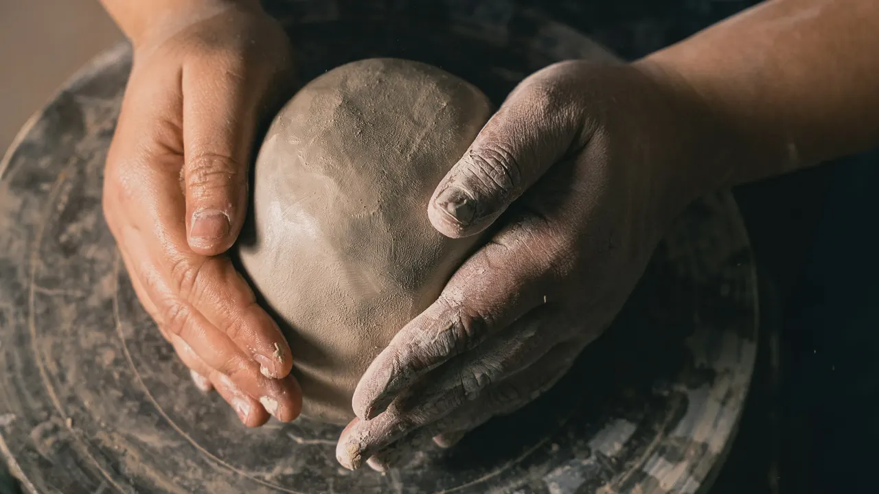 Hands shaping clay on a pottery wheel