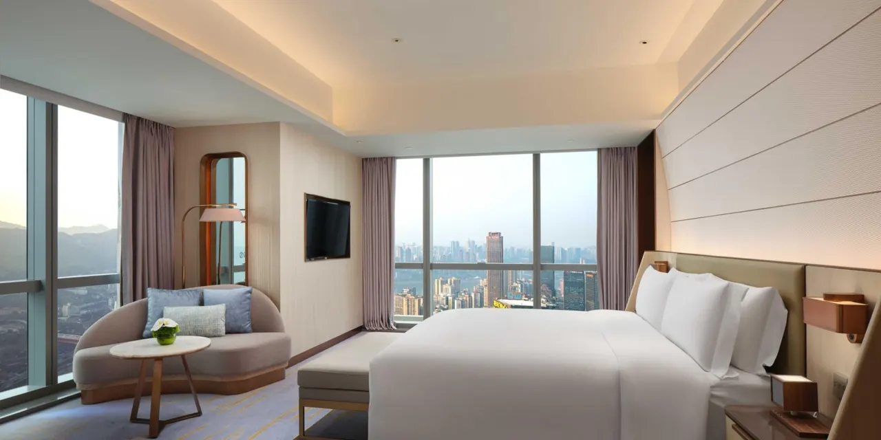 Corner room with a large bed, curved sofa and tall windows looking over the river and city.