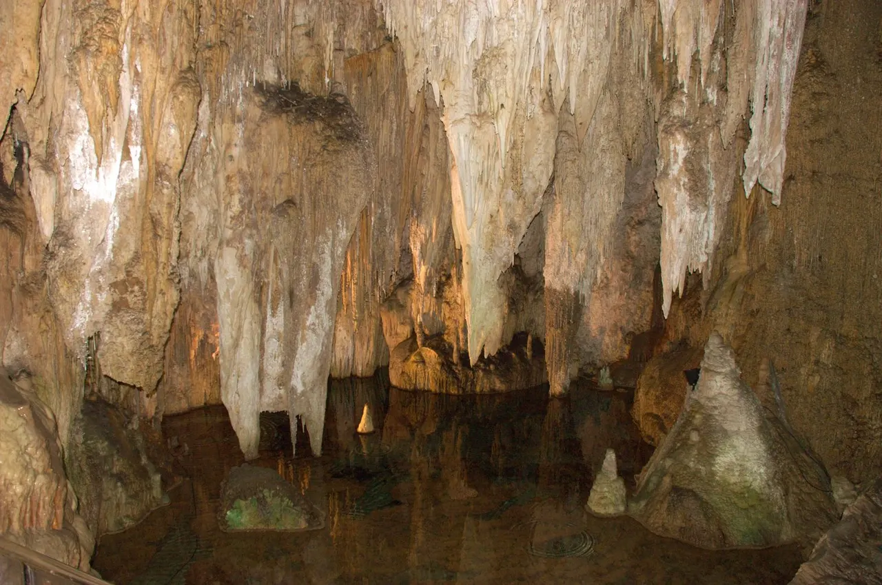 Stalactites and stalagmites beside shallow water inside Furong Cave