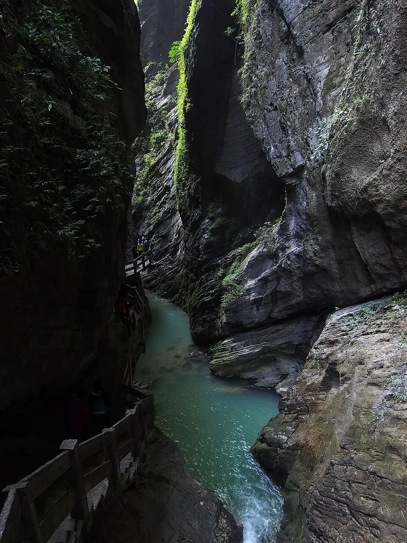 A fenced walkway beside a green stream between the narrow cliffs of Longshuixia