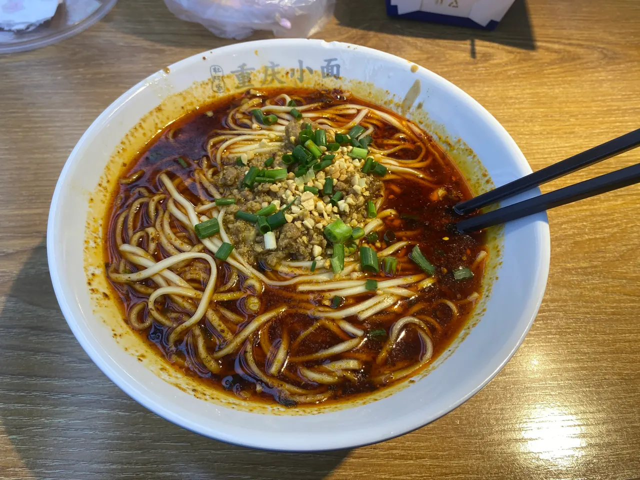 Bowl of spicy wheat noodles topped with chili oil, ground meat, peanuts, and scallions.